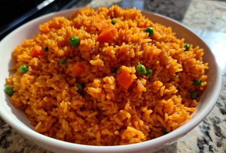 A close-up shot of a white bowl filled with fluffy, bright orange spanish rice mixed with green peas and diced carrots.