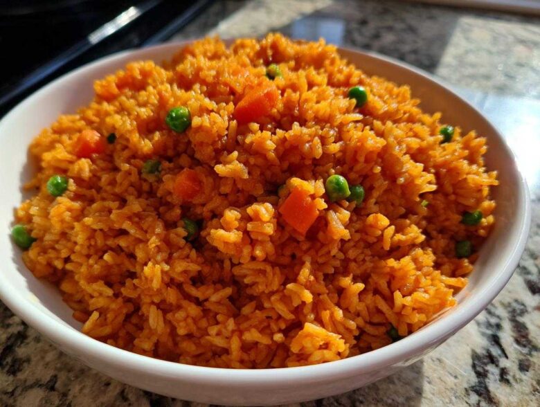 A close-up shot of a white bowl filled with fluffy, bright orange spanish rice mixed with green peas and diced carrots.