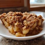 A close-up of a warm slice of apple crisp showing gooey filling and a thick, crunchy oat topping.