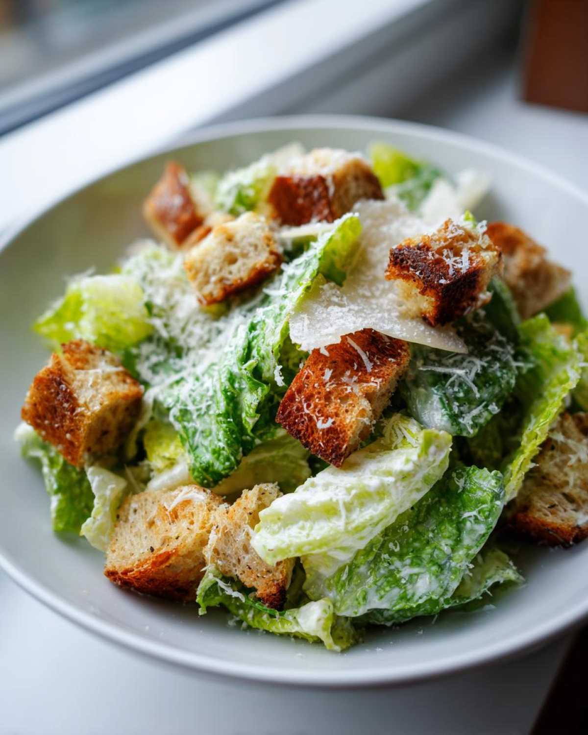 A close-up of a fresh caesar salad featuring crisp romaine lettuce, golden croutons, and shaved Parmesan cheese.