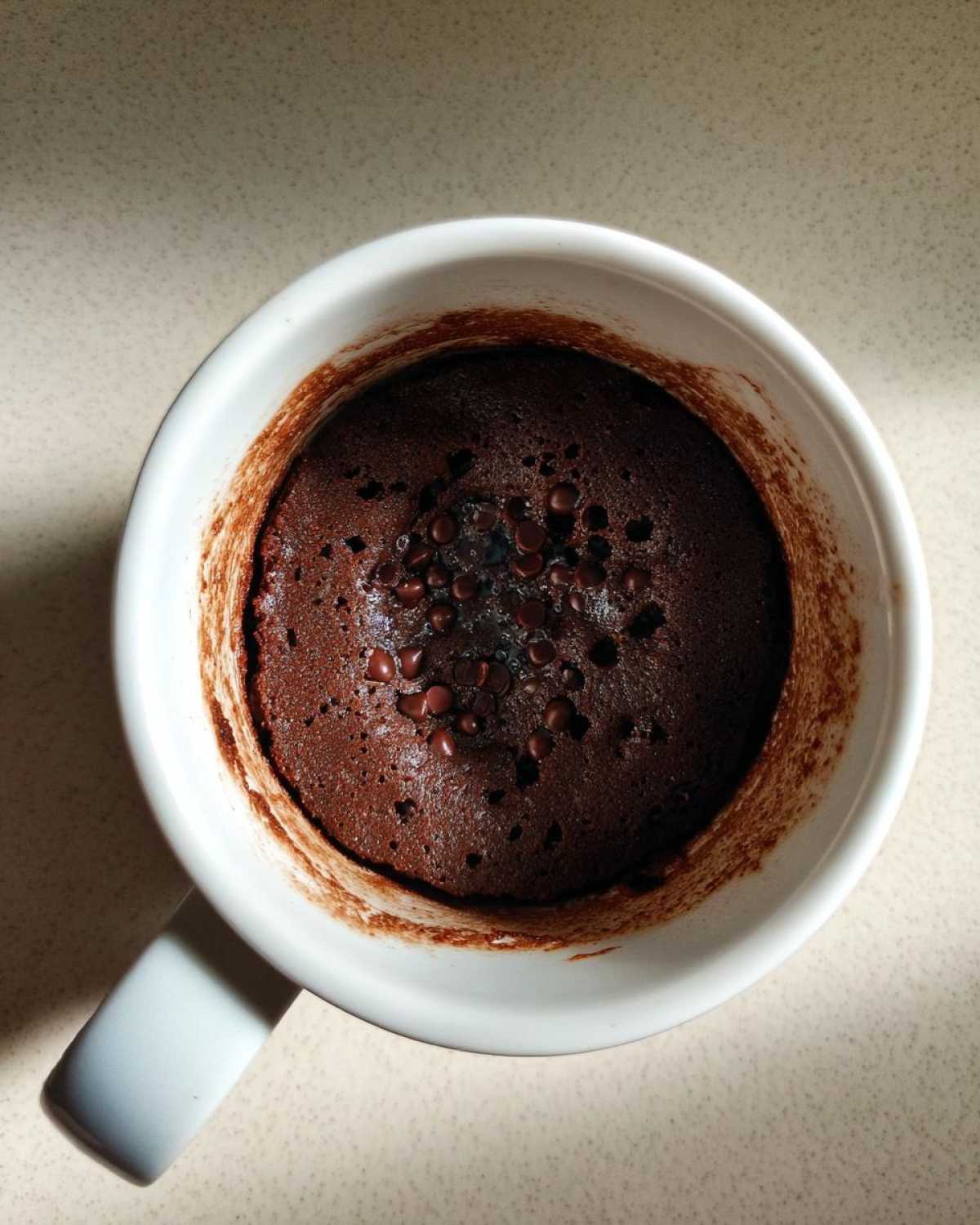 Overhead view of a rich, dark chocolate mug cake topped with melted chocolate chips, fresh from the microwave.