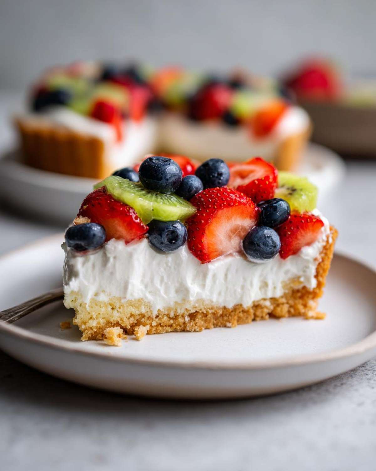 Close-up of a slice of fruit pizza sugar cookie dessert with strawberries, blueberries, and kiwi on cream cheese frosting.