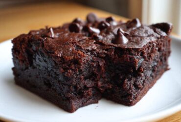 Close-up of a rich, fudgy slice of black bean brownies topped with chocolate chips on a white plate.