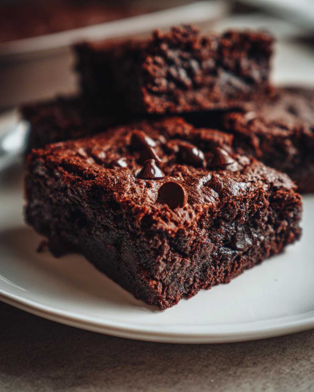 Close-up of a fudgy square of black bean brownies topped with chocolate chips on a white plate.