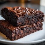 Two stacked, fudgy black bean brownies topped with melted chocolate chips on a white plate.
