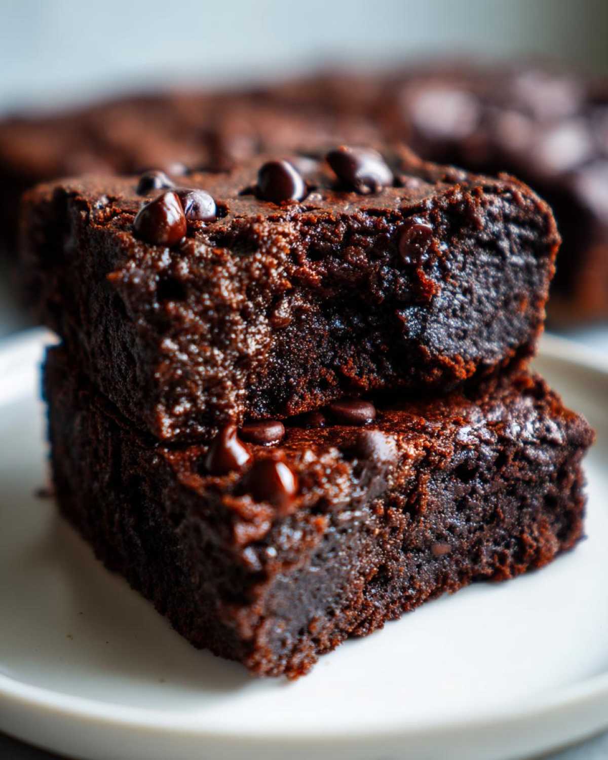 Close-up of two fudgy black bean brownies stacked on a white plate, topped with melted chocolate chips.