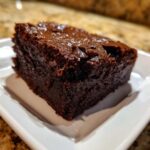A close-up shot of a thick, fudgy square of sweet potato brownies on a small white plate.