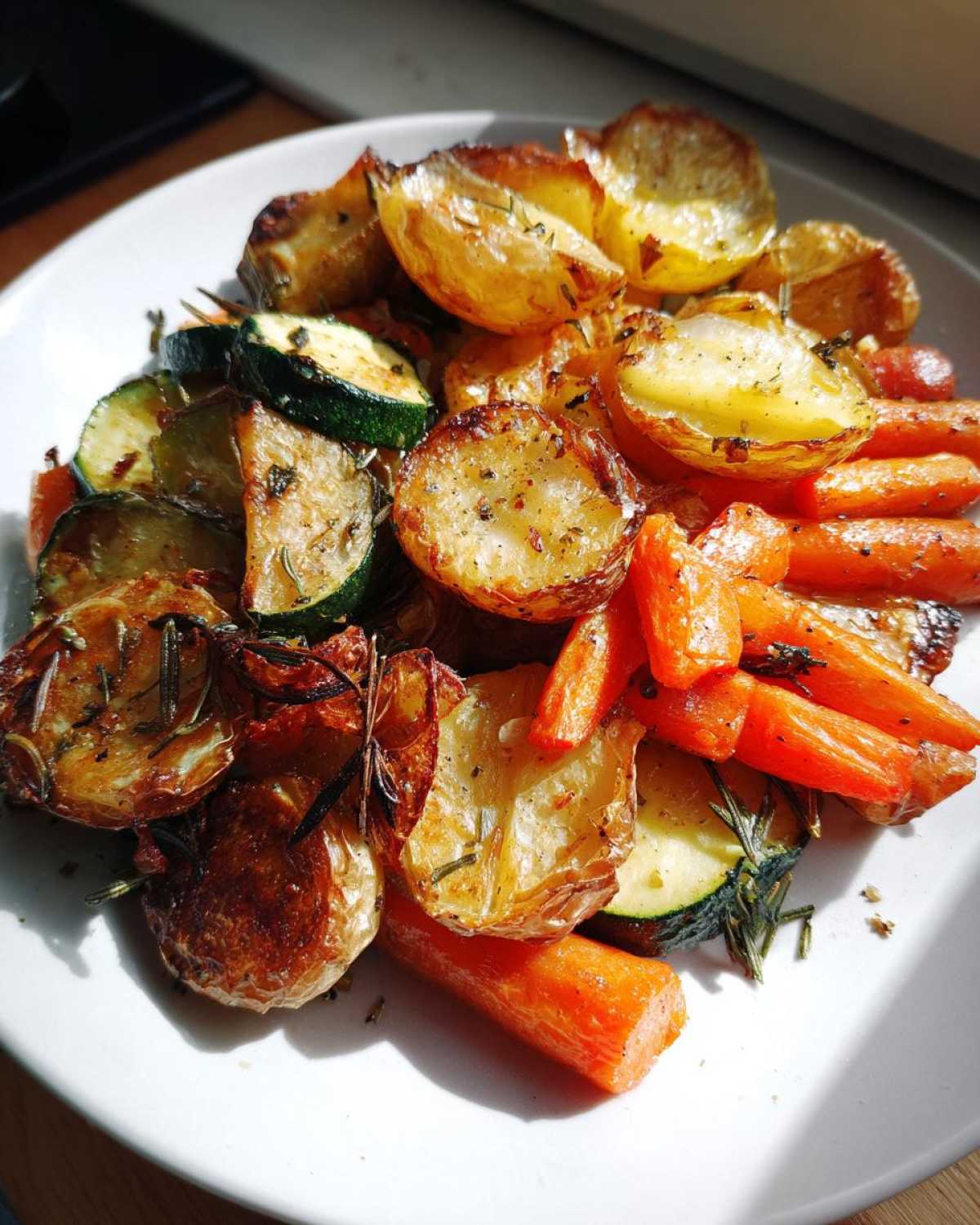 A plate piled high with golden brown Garlic Herb Roasted Veggies, including potatoes, carrots, and zucchini, seasoned with herbs.