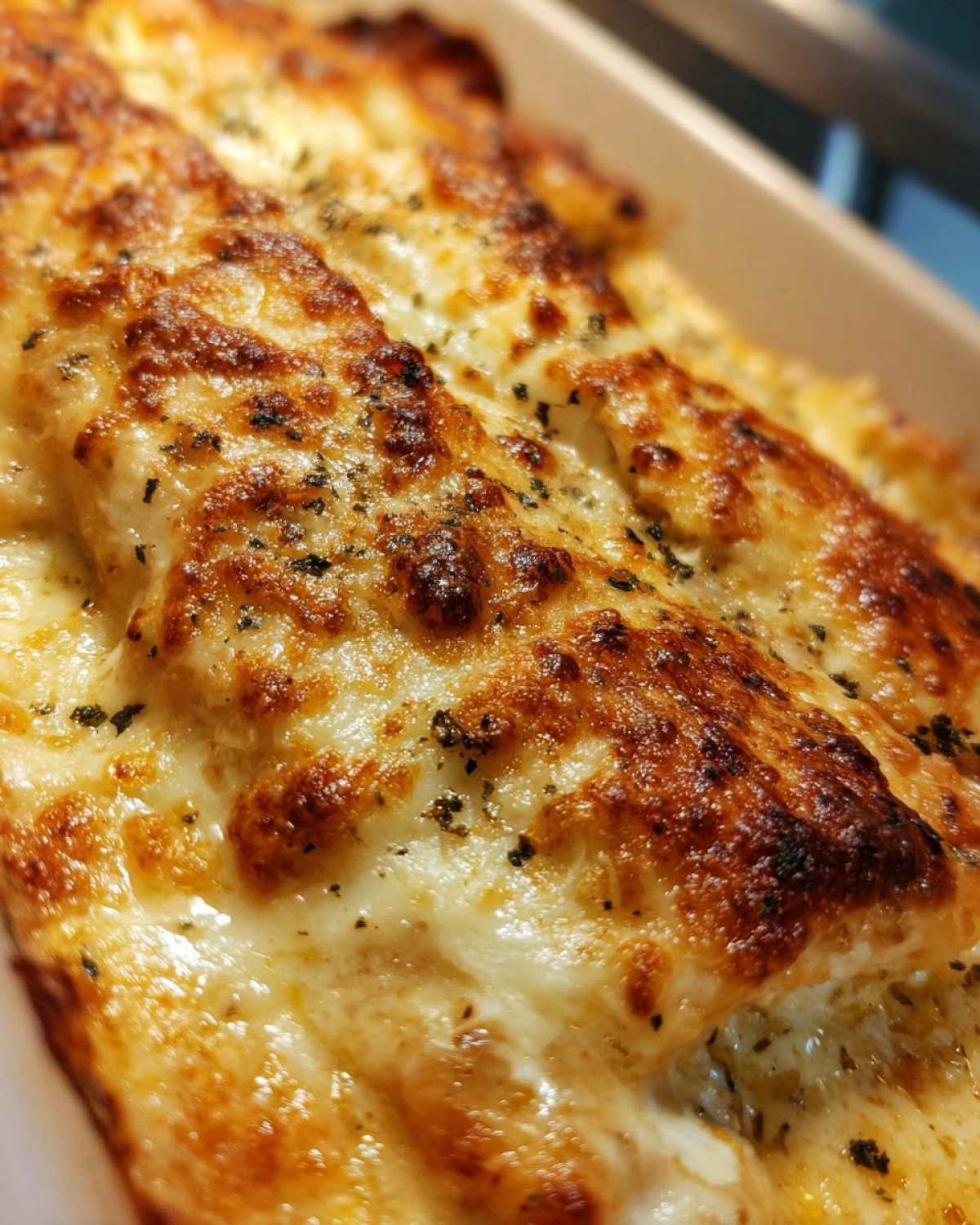 Close-up of a bubbly, golden-brown cheese topping on a Garlic parmesan chicken bake, sprinkled with herbs.