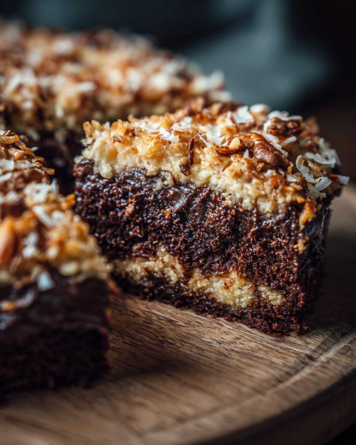 Close-up of a rich slice of german chocolate poke cake showing moist chocolate cake layers and a toasted coconut pecan topping.