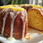 A glazed lemon pound cake, featuring a slice cut out to show the moist interior, topped with lemon slices.