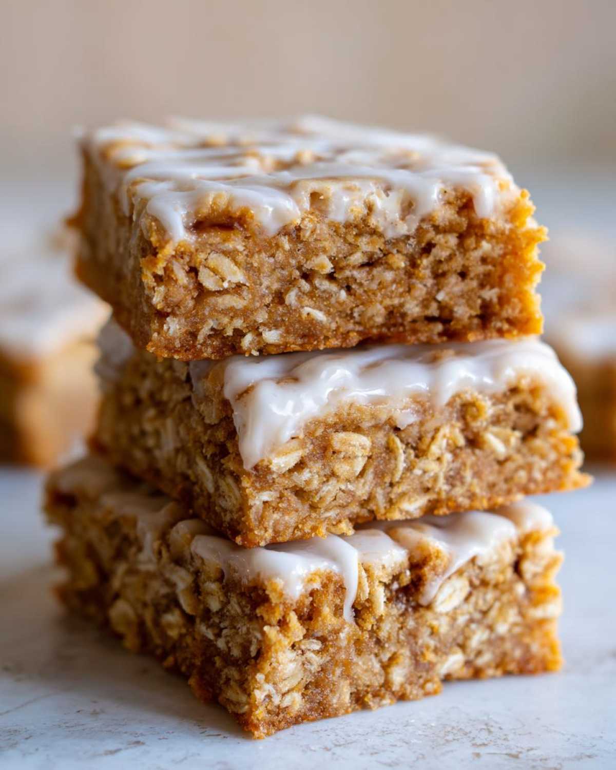 A stack of three thick, chewy oatmeal bars topped with a sweet white glaze.