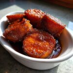 Close-up of thick-cut candied sweet potatoes glistening with rich brown syrup in a white bowl.
