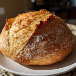 A perfectly baked, round loaf of Italian bread with a deeply browned, crackled crust dusted with flour.