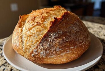 A perfectly baked, round loaf of Italian bread with a deeply browned, crackled crust dusted with flour.