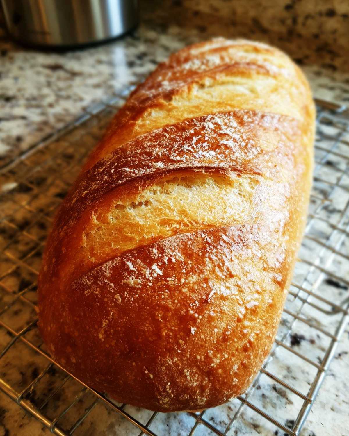 A golden brown, freshly baked loaf of french bread resting on a wire cooling rack.