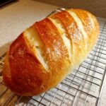 A freshly baked loaf of golden brown french bread cooling on a wire rack.