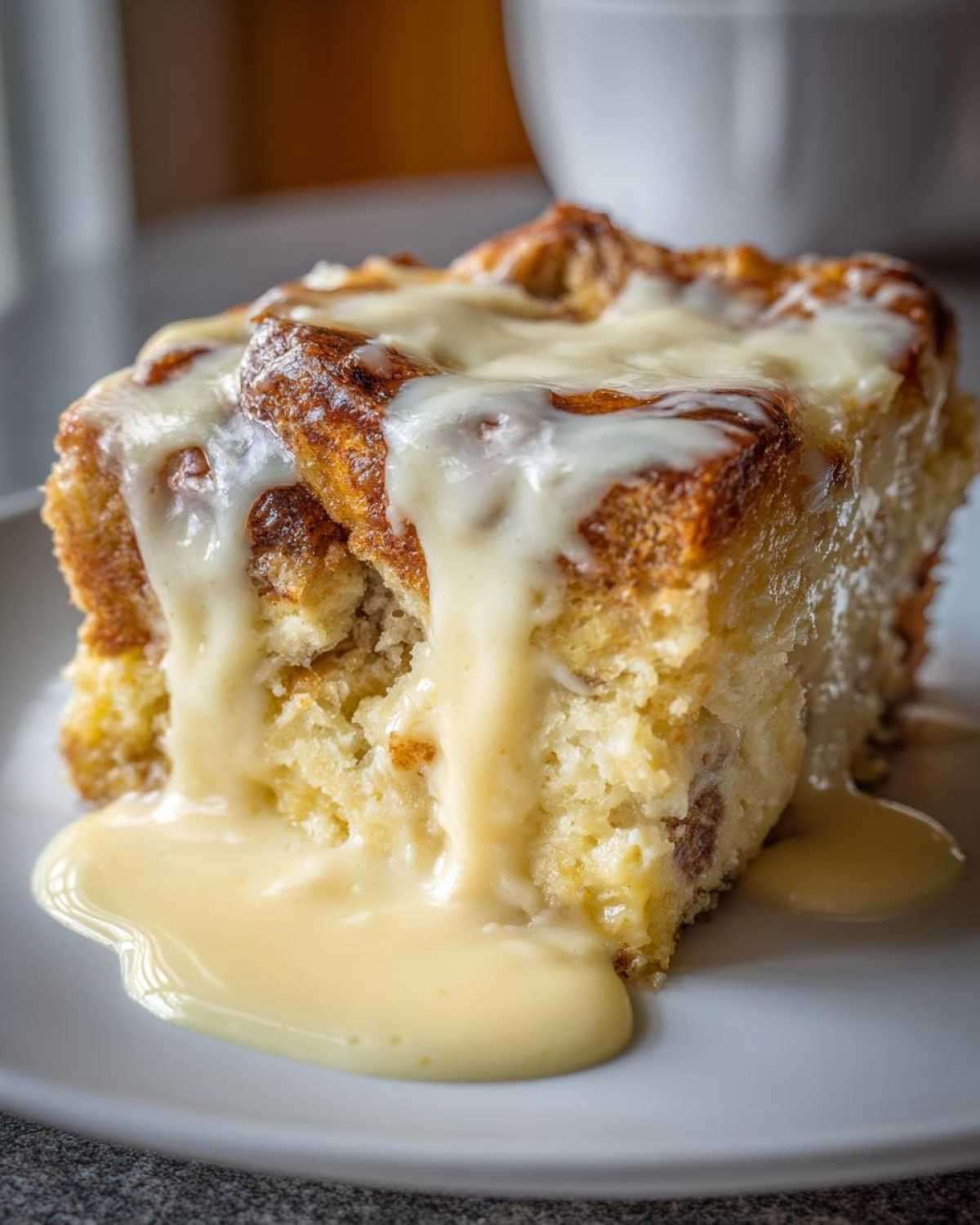Close-up of a warm, square slice of bread pudding generously topped with thick, dripping vanilla sauce.