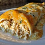A close-up view of two green chile chicken enchiladas covered in melted orange and white cheese on a white plate.