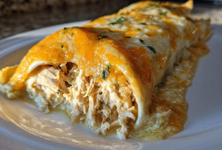 A close-up view of two green chile chicken enchiladas covered in melted orange and white cheese on a white plate.