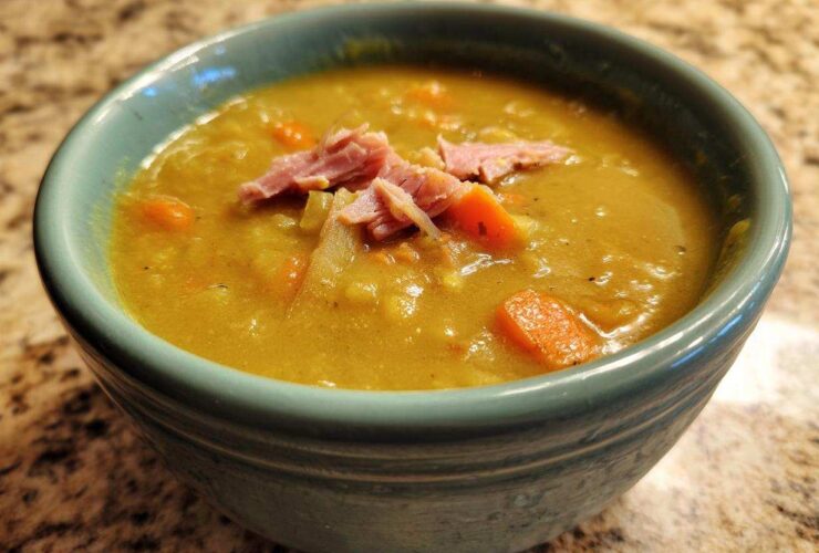 Close-up of a thick, yellow-green pea soup topped with shredded ham and carrots in a teal bowl.