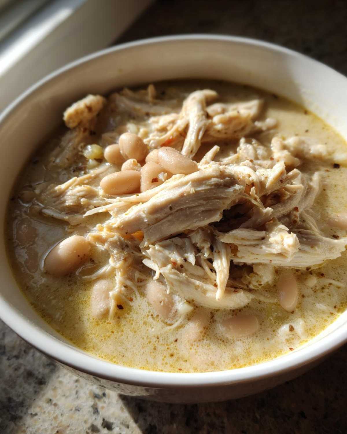 A close-up of a bowl of creamy white chicken chili topped with shredded white chicken and white beans.