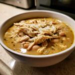 Close-up of a hearty bowl of white chicken chili, featuring shredded white chicken, beans, and melted cheese.