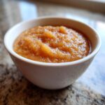 Close-up of chunky, homemade applesauce seasoned with cinnamon served in a small white bowl.