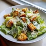 A close-up of a fresh caesar salad tossed in creamy dressing, topped with golden croutons and grated Parmesan cheese.