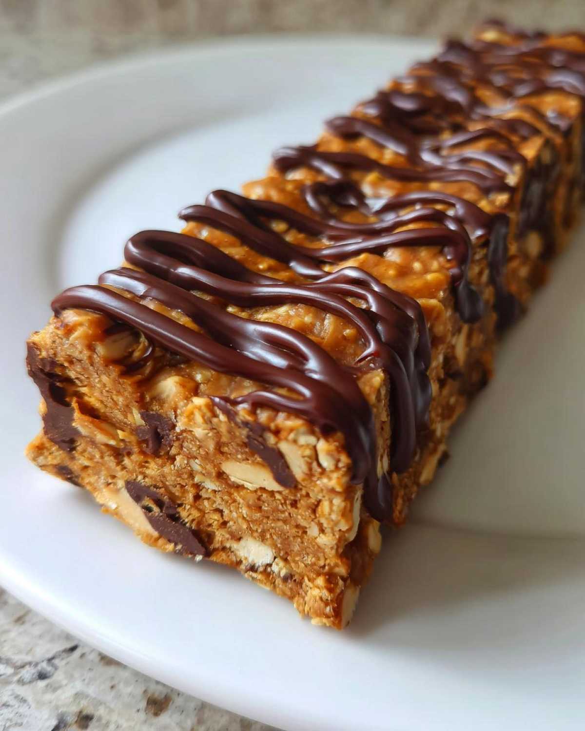 A close-up of a homemade, peanut butter-colored protein bars drizzled generously with dark chocolate.