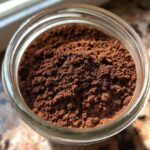 Overhead view of rich, dark brown homemade hot cocoa mix powder filling a clear glass jar.