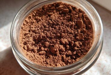 Close-up overhead view of rich brown homemade hot cocoa mix powder stored in a clear glass jar.