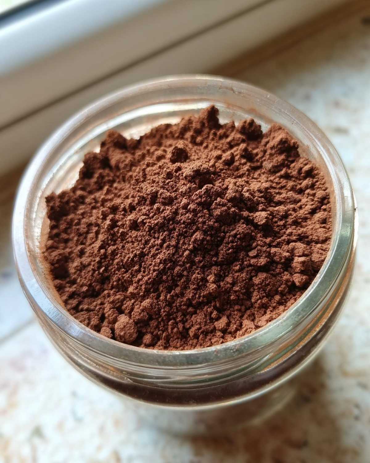 Close-up overhead view of rich brown homemade hot cocoa mix powder filling a clear glass jar.