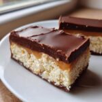A delicious, layered homemade twix bar slice showing a shortbread base, caramel, and thick chocolate topping.