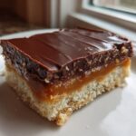 A single, thick slice of homemade Twix bar showing the shortbread base, gooey caramel layer, and chocolate topping.