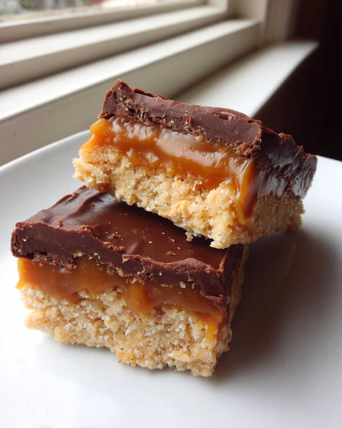 Two stacked homemade Twix bars showing the shortbread base, thick caramel, and chocolate topping.