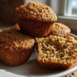 Close-up of three golden brown honey bran muffins, one cut in half showing the moist interior texture.