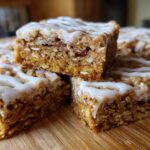 A stack of moist, square oatmeal bars topped with a thick white glaze, ready to be served.