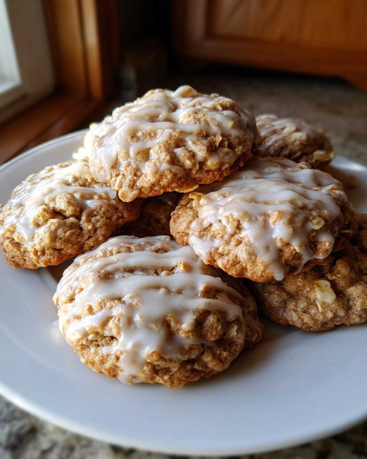 A stack of freshly baked iced oatmeal cookies drizzled with a thick vanilla glaze, resting on a white plate.