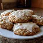 A stack of soft, freshly baked iced oatmeal cookies topped with a thick, white glaze on a white plate.