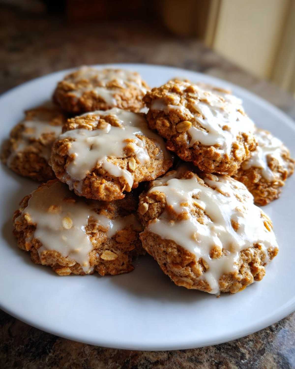 A close-up of several soft, glazed iced oatmeal cookies piled on a white plate.