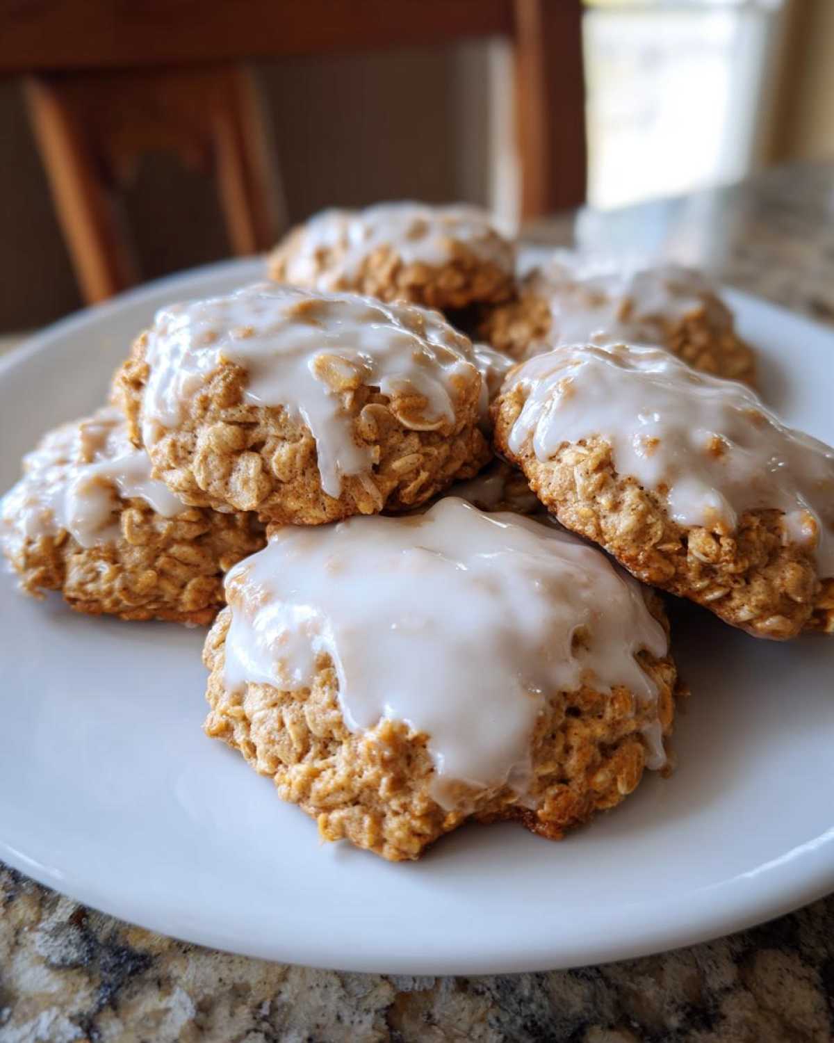 A close-up of several soft iced oatmeal cookies piled on a white plate.