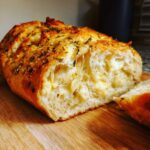 A close-up of freshly baked Italian herb and cheese bread, showing a gooey, cheesy interior and herb-topped crust.