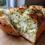 A freshly baked loaf of Italian herb and cheese bread pulled apart to show melted cheese and herbs inside.