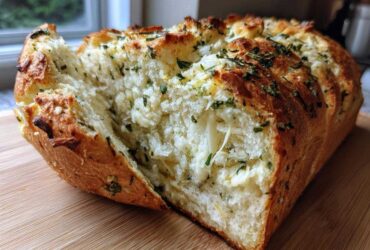 A freshly baked loaf of Italian herb and cheese bread pulled apart to show melted cheese and herbs inside.