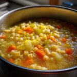 Close-up of hot italian penicillin soup with ditalini pasta, carrots, celery, and lemon zest in a metal pot.