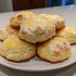 A stack of freshly baked Italian ricotta cookies topped with a bright yellow glaze and white icing drizzle.
