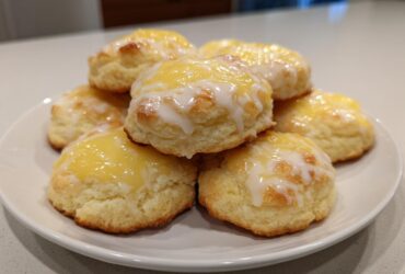 A stack of freshly baked Italian ricotta cookies topped with a bright yellow glaze and white icing drizzle.