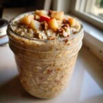 Close-up of apple cinnamon overnight oats in a mason jar, topped with diced apples and pecans.