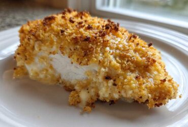 Close-up of a juicy caesar chicken breast with a thick, golden, crispy breadcrumb coating served on a white plate.